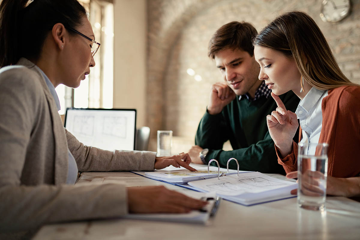 Young man and his wife examining housing plans with real estate agent on a meeting in the office.